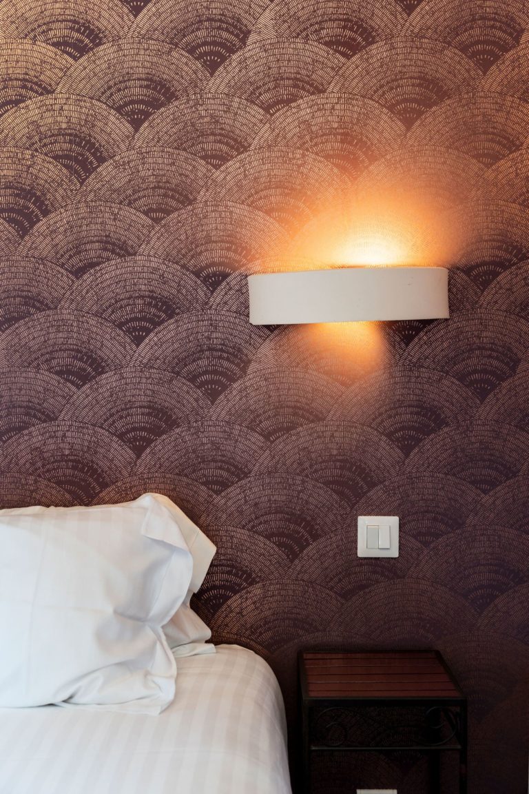 Détail d'une chambre rénovée d'un hôtel des années 30 avec un papier peint art déco et des touches de rose, conçu par JoyDesign Intérieur.