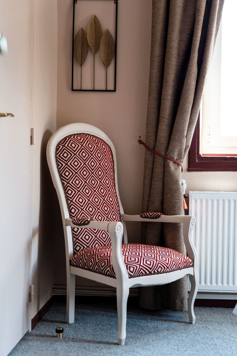 Fauteuil rénové d'un hôtel des années 30 avec un tissu à motifs géométriques rouges et blancs, conçu par JoyDesign Intérieur.