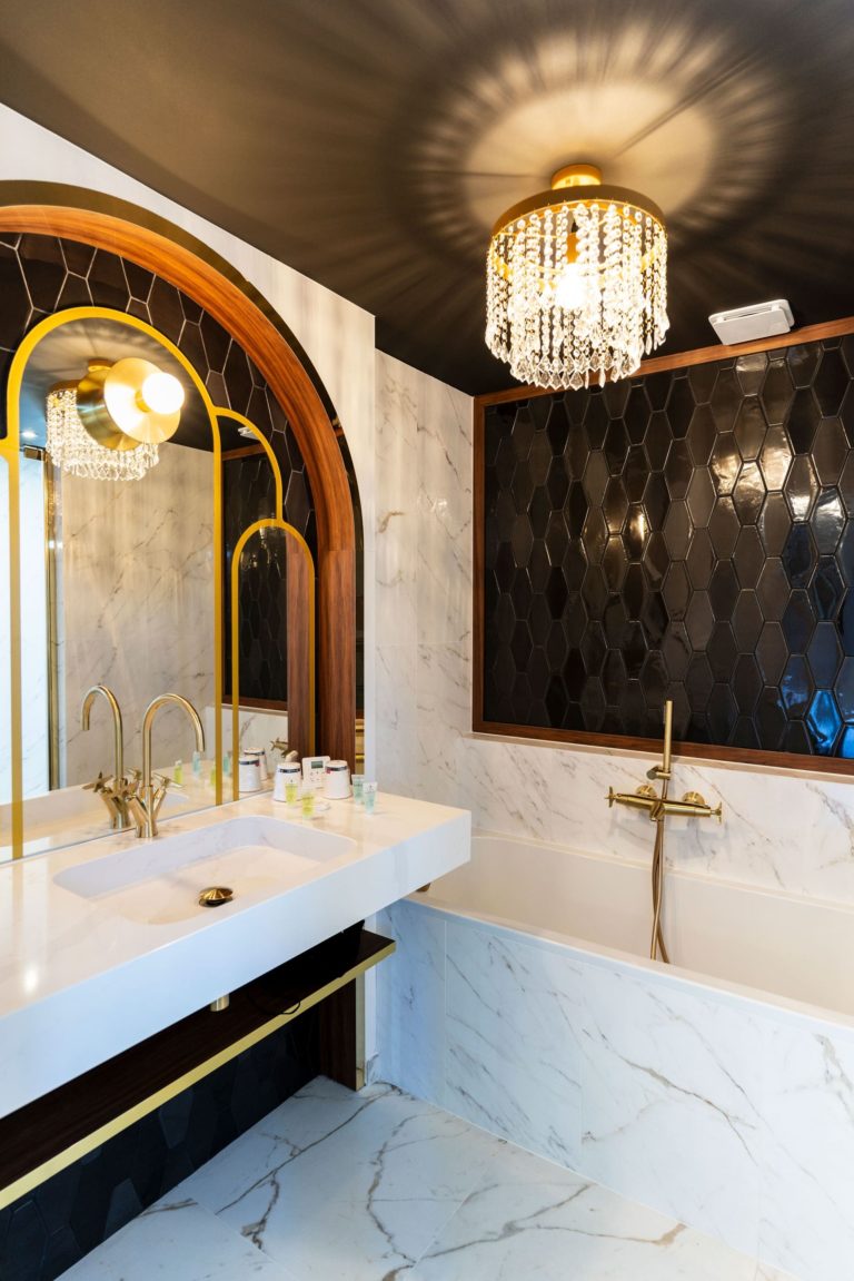 Salle de bain rénovée d'un hôtel des années 30 avec des finitions en marbre, des accents dorés, et des carreaux noirs, conçue par JoyDesign Intérieur.