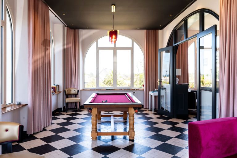 Salle de jeux rénovée d'un hôtel des années 30 avec une table de billard, des rideaux roses et un sol en damier, conçue par JoyDesign Intérieur.