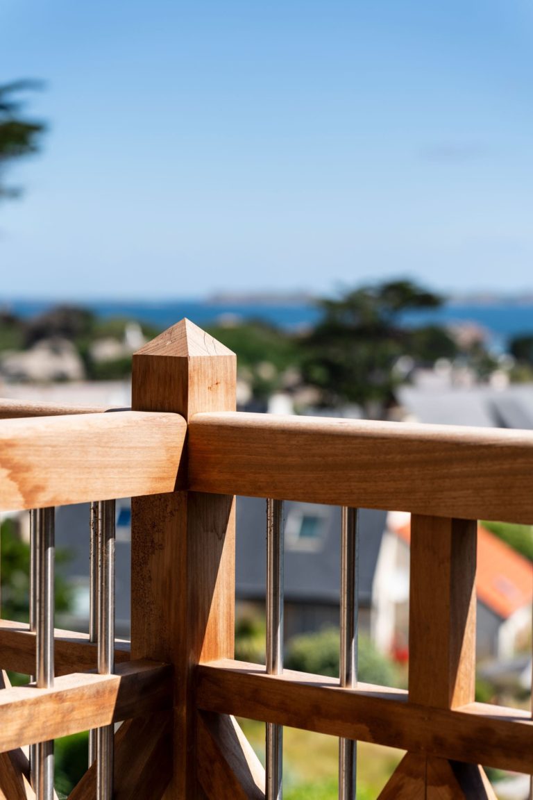 Gros plan sur la balustrade en bois avec vue sur la mer depuis un balcon rénové d'un hôtel à Trégastel, conçu par JoyDesign Intérieur.