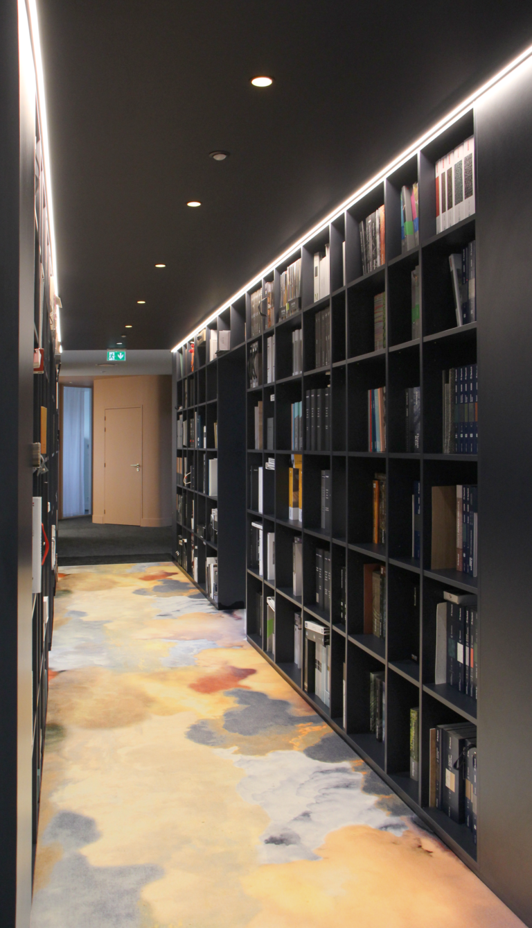 Couloir des bureaux de Joydesign Intérieur avec des étagères remplies de livres et un sol au design artistique.
