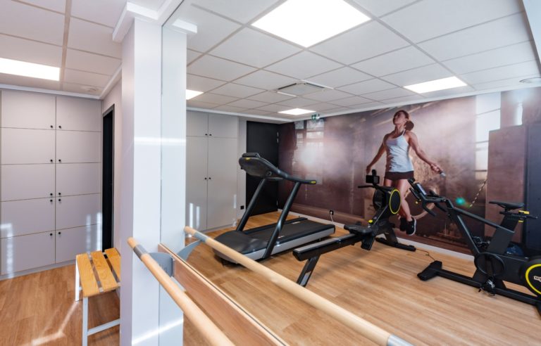 Salle de sport avec tapis de course, vélos d'appartement et mur décoratif, conçue par JoyDesign Intérieur pour un cabinet d'avocat