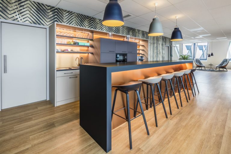 Bar moderne et élégant avec des tabourets hauts et des étagères ouvertes dans des bureaux, conçu par JoyDesign Intérieur.