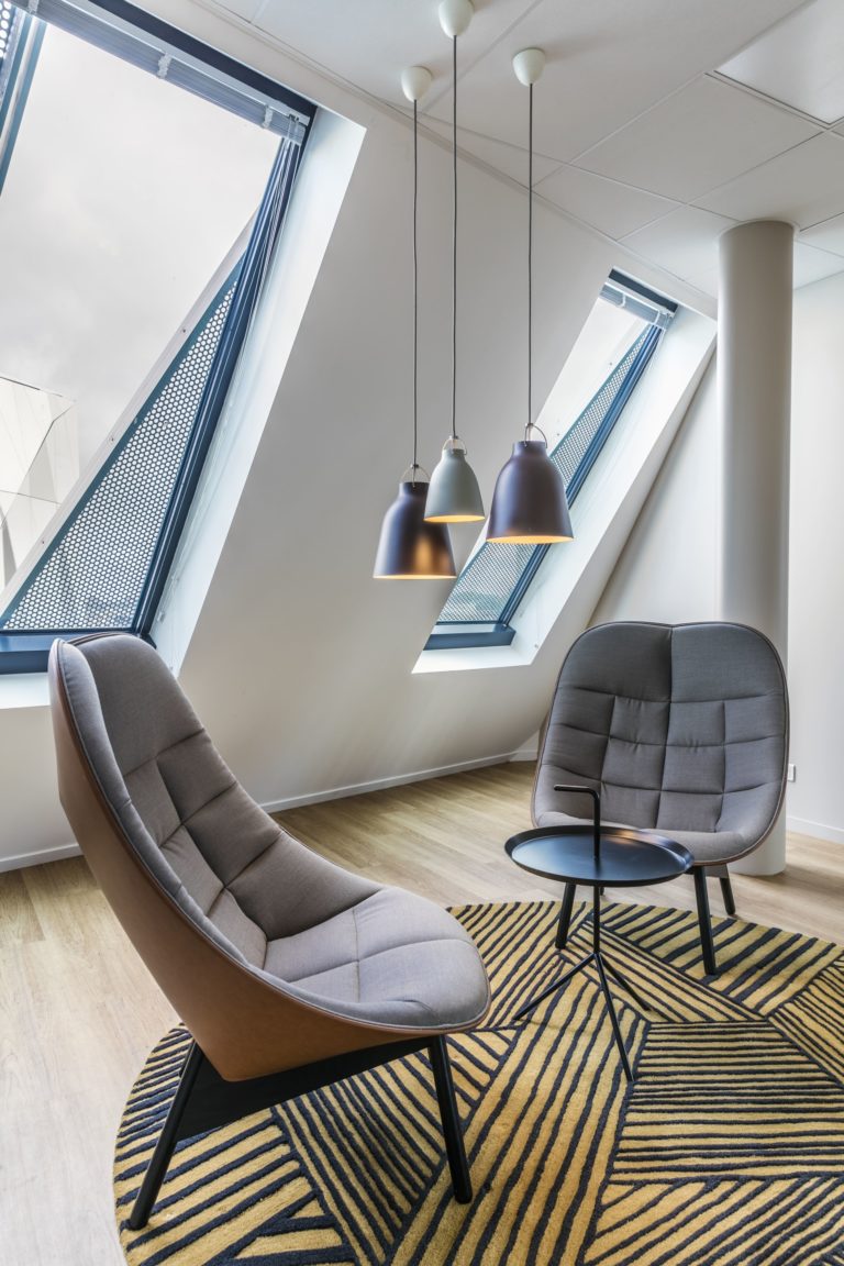 Coin détente avec fauteuils gris et luminaires suspendus dans des bureaux modernes, conçu par JoyDesign Intérieur.