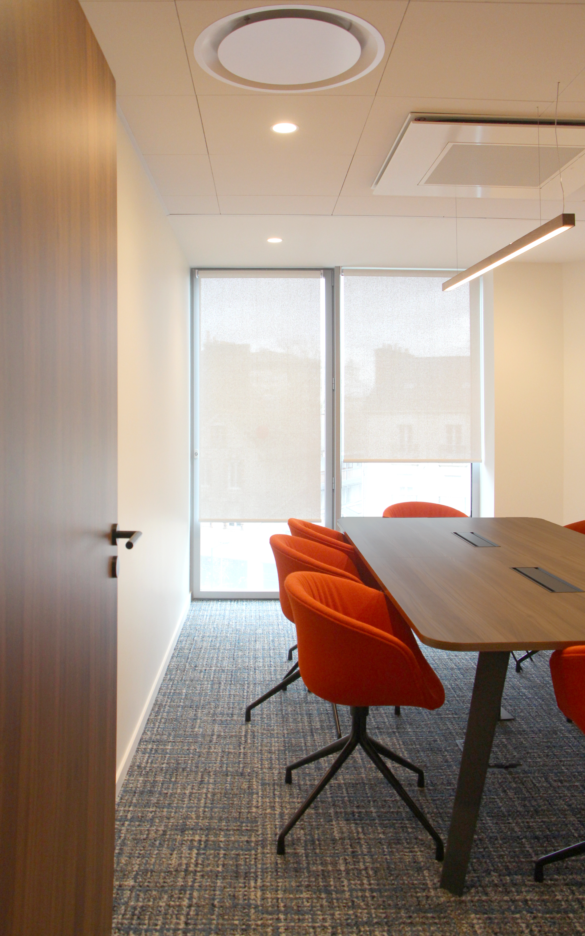 Salle de réunion lumineuse dans des bureaux de 700m², équipée de chaises orange et d'une grande table en bois, conçue par JoyDesign Intérieur.