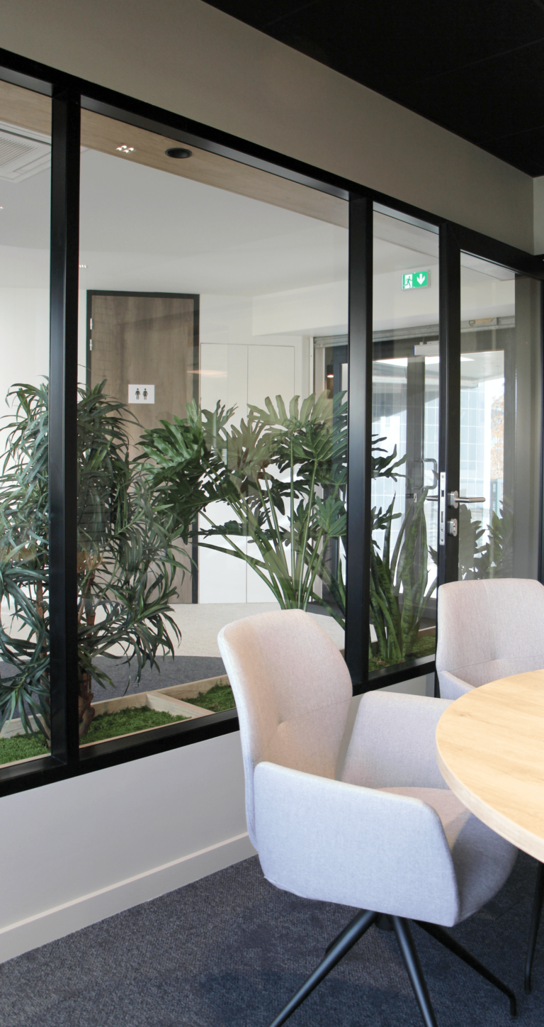 Espace de réunion dans des bureaux modernes, avec vue sur une zone de plantes d'intérieur.