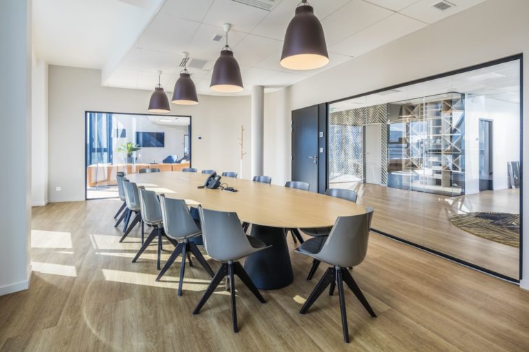 Salle de réunion lumineuse avec grande table ovale et chaises grises dans des bureaux modernes, conçu par JoyDesign Intérieur.