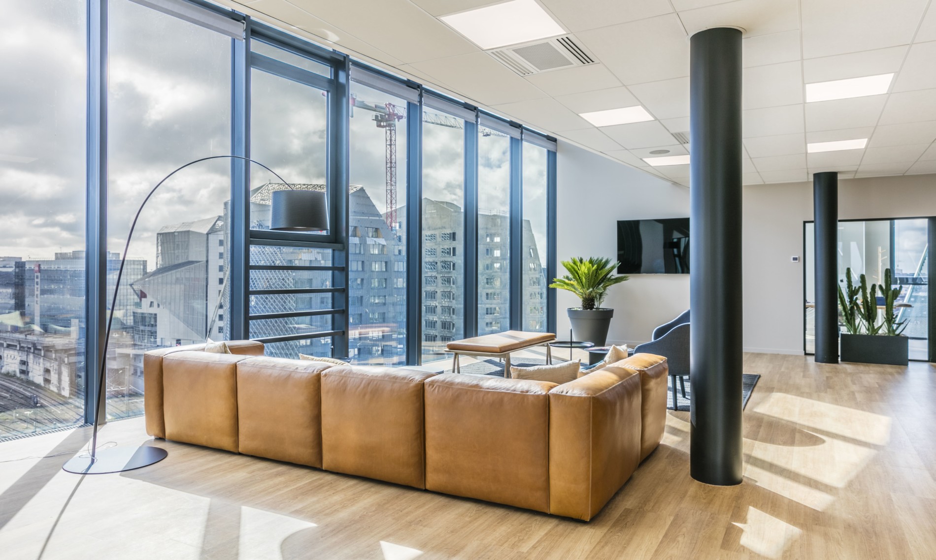 Espace détente lumineux avec canapé en cuir et vue panoramique dans des bureaux, conçu par JoyDesign Intérieur.