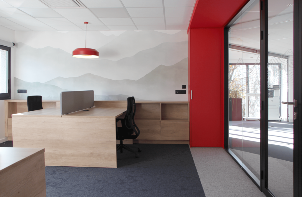 Bureaux modernes avec séparateurs, éléments en bois clair, et accent rouge.