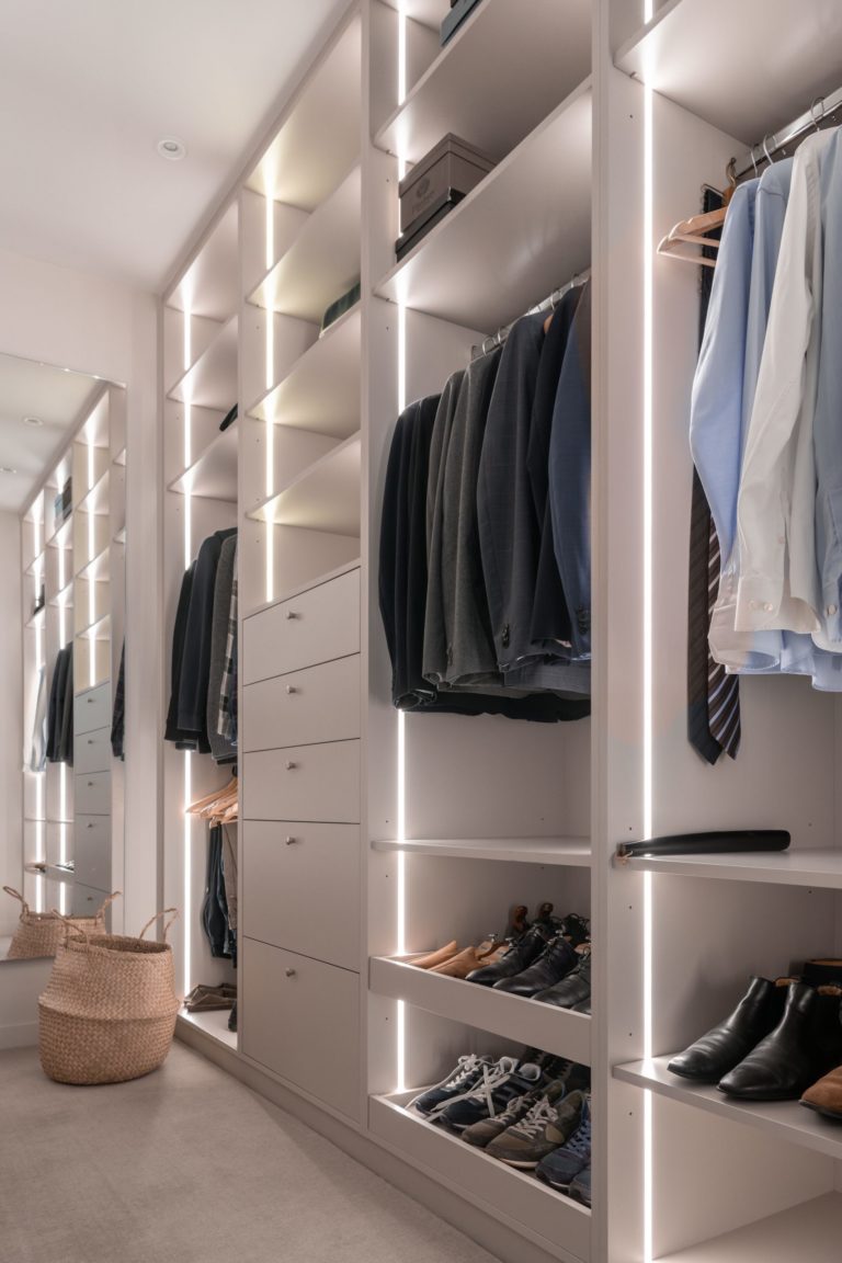 Un dressing spacieux et bien organisé avec des éclairages intégrés, des étagères et des tiroirs, contenant des vêtements et des chaussures.