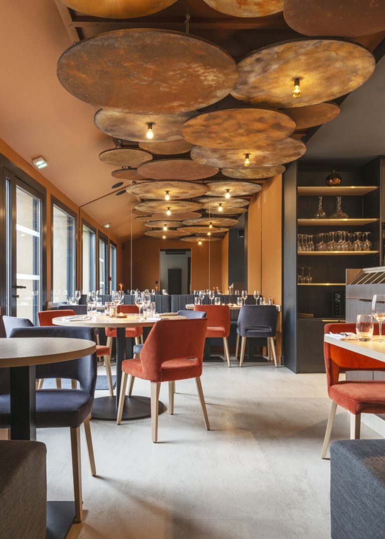 Salle de restaurant chaleureuse avec des tons chauds et un plafond en acier corten, conçue par JoyDesign Intérieur pour évoquer la chaleur des flammes.