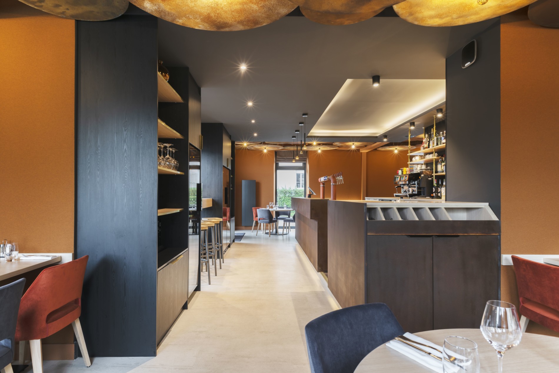 Intérieur d'un restaurant avec des tons chauds et un bar en acier corten, conçu par JoyDesign Intérieur pour évoquer la chaleur des flammes.