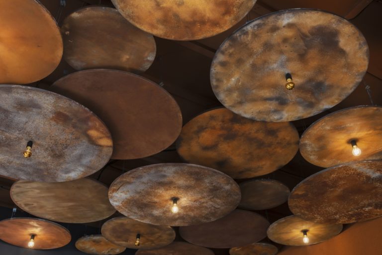 Détail du plafond en acier corten avec des luminaires dans le restaurant L'Âtre à Rennes, conçu par JoyDesign Intérieur pour évoquer la chaleur des flammes.