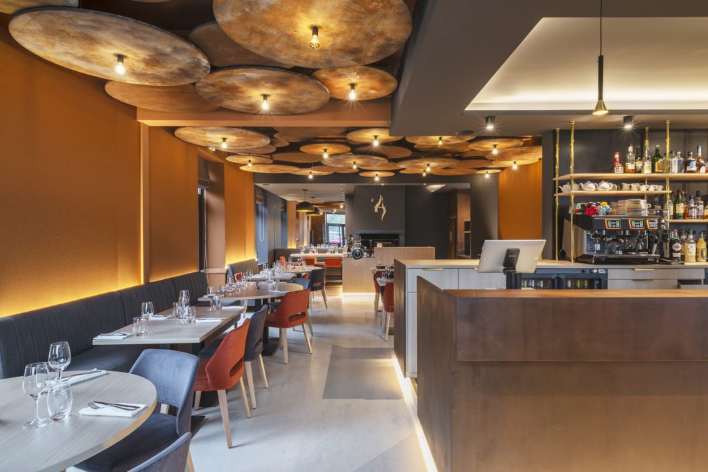 Intérieur du restaurant L'Âtre à Rennes avec des tons chauds et un plafond en acier corten, conçu par JoyDesign Intérieur pour évoquer la chaleur des flammes.