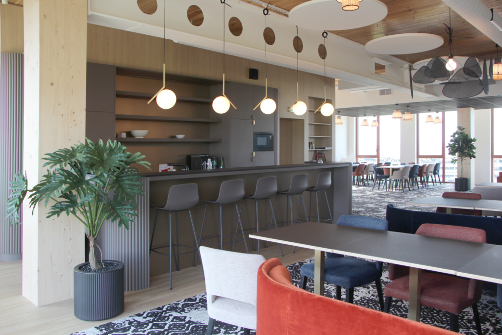 Photo d'un espace intérieur moderne et élégant d'une agence d'architecture avec un bar, des luminaires suspendus, et des tables et chaises colorées.