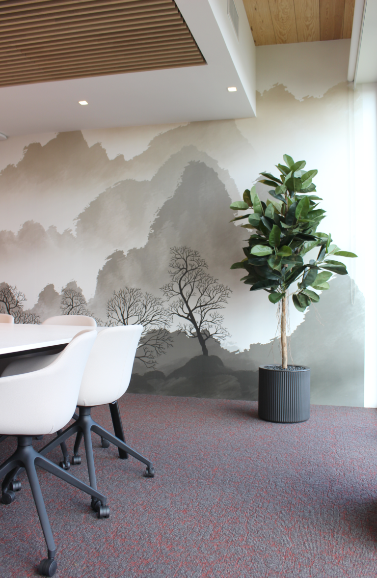 Salle de réunion moderne avec une fresque murale de paysage naturel, des chaises blanches et une plante en pot.