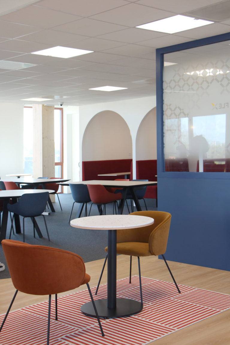 Espace de réunion avec des chaises colorées, une table ronde en marbre, un mur bleu et des arches décoratives.