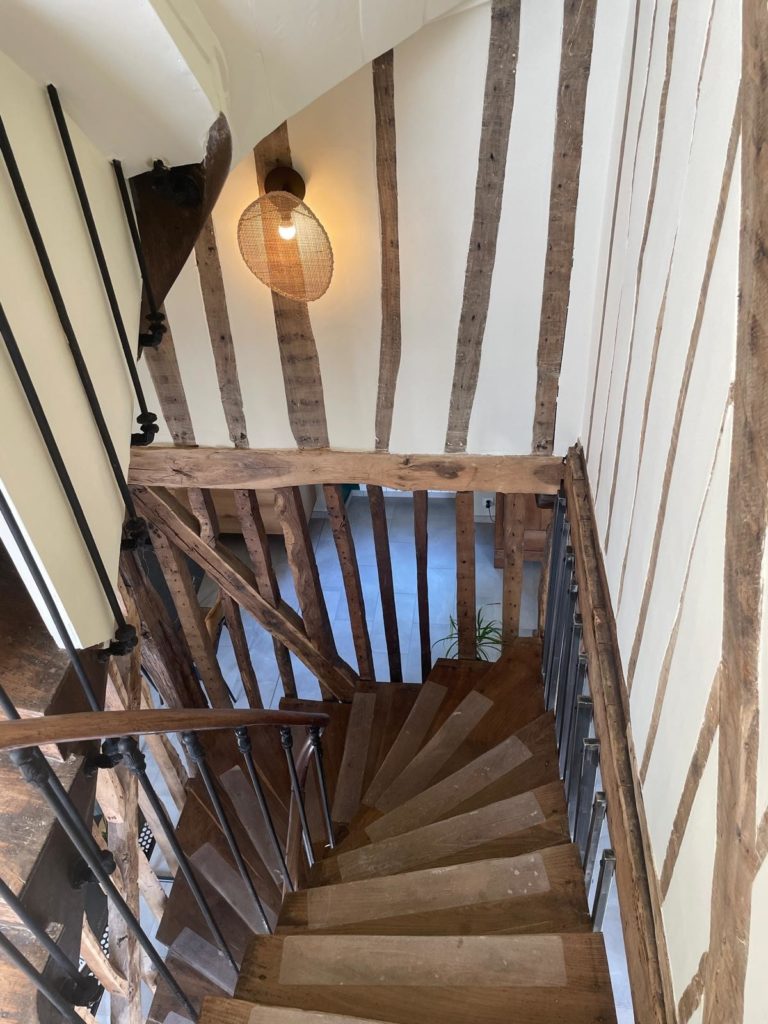 Cage d'escalier en bois avec des poutres apparentes et une rampe en métal.