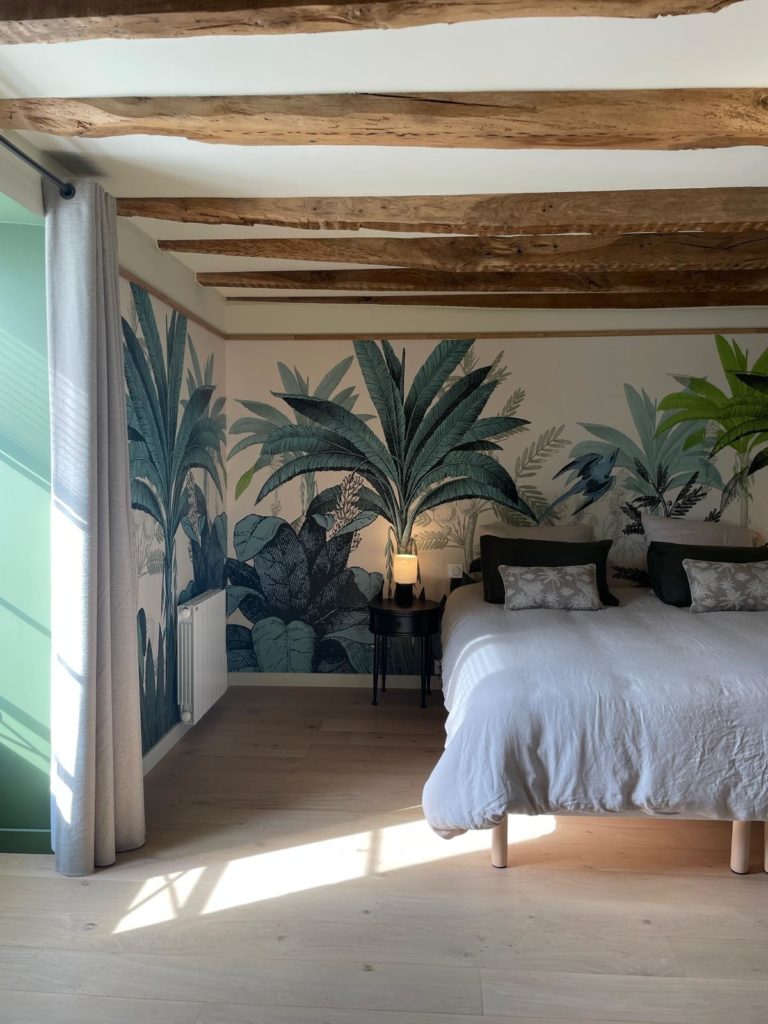 Chambre avec poutres en bois apparentes, décorée avec une fresque murale tropicale et des accents verts.