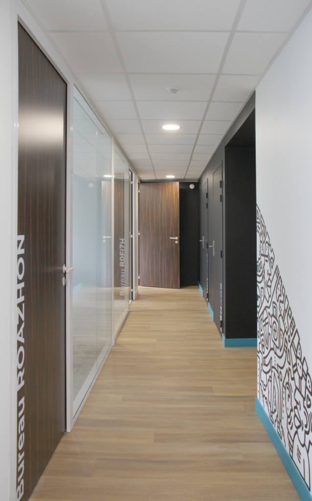 Couloir de bureaux avec décoration artistique et portes en bois.